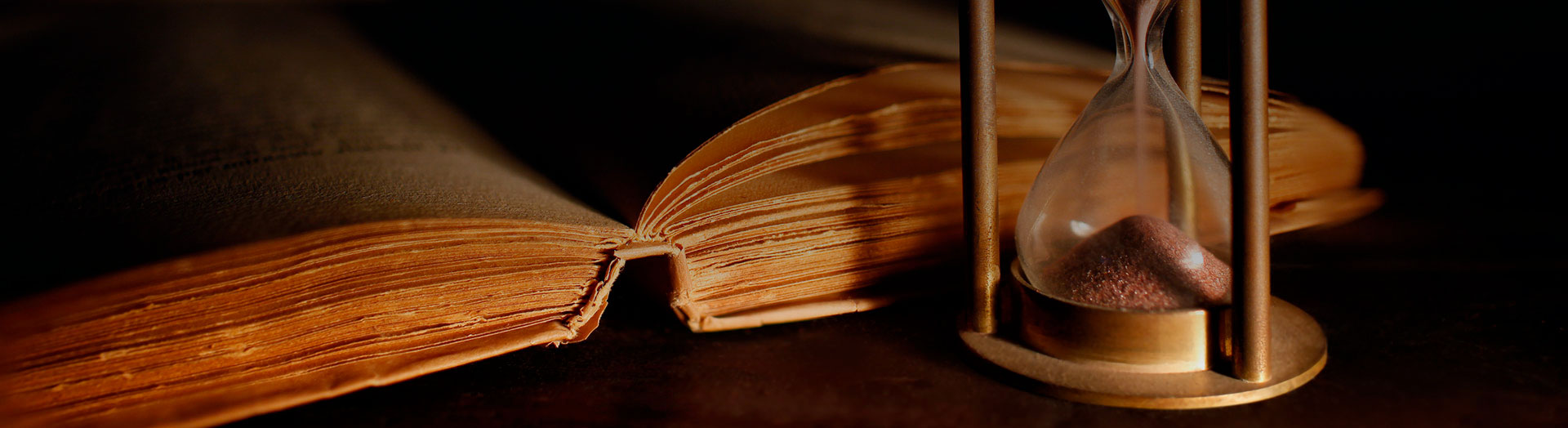 Sobre la mesa se muestra una libro grueso abierto y un reloj de arena