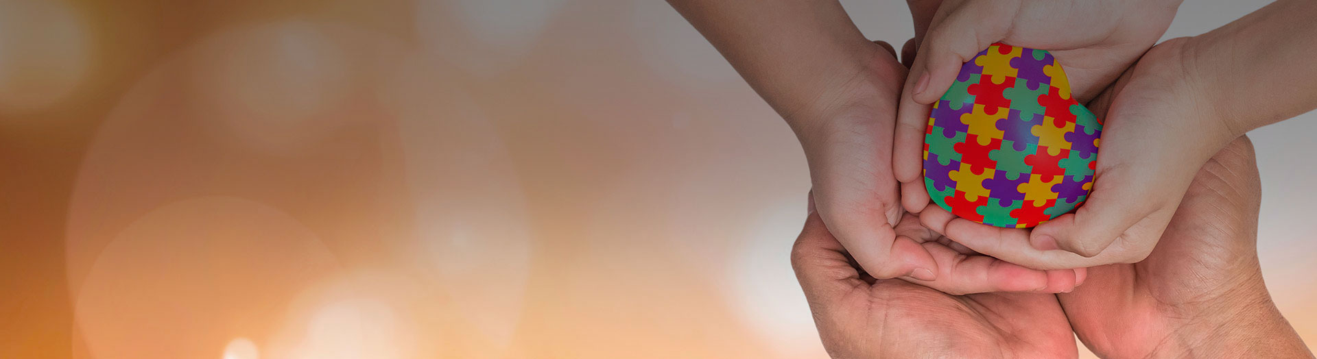 Manos unidas sostiene un corazón de colores, formado de piezas de rompecabezas