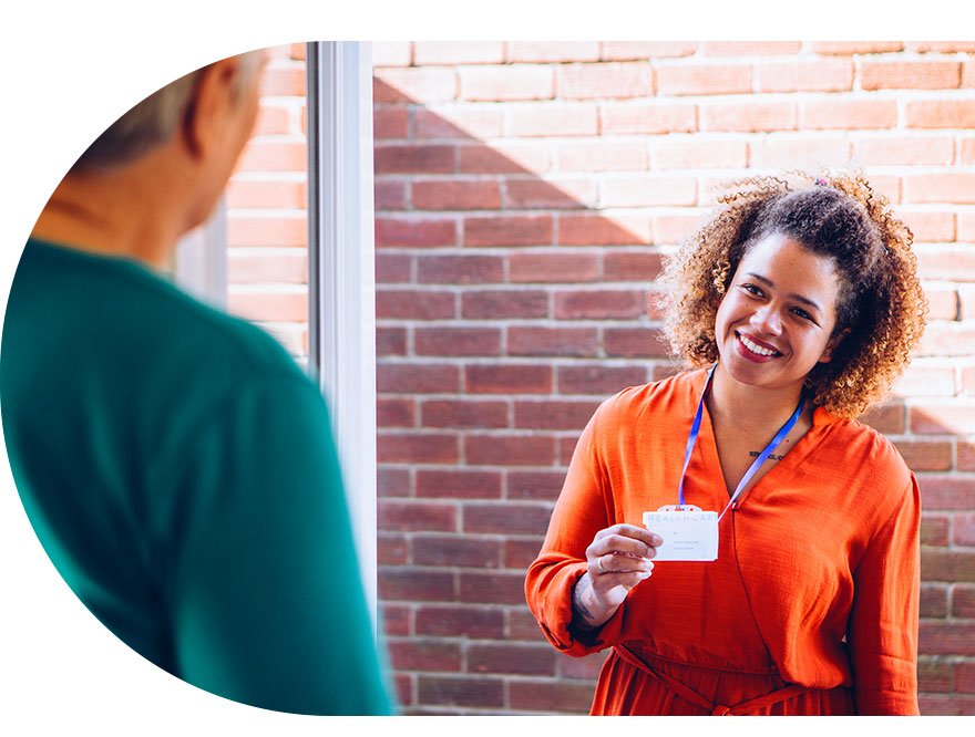 Trabajadora social saluda por la puerta de una casa, ella está sonriendo