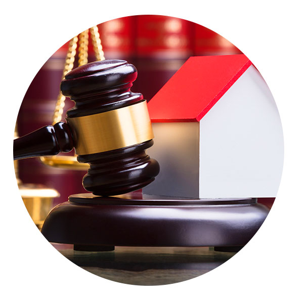 Sobre una mesa se muestra una balanza, una casa y un mazo de un juez