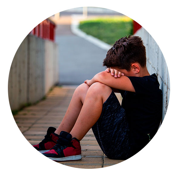 Niño sentado en el suelo, triste, sus manos recogen sus piernas y su cabeza toca sus rodillas para taparse la cara