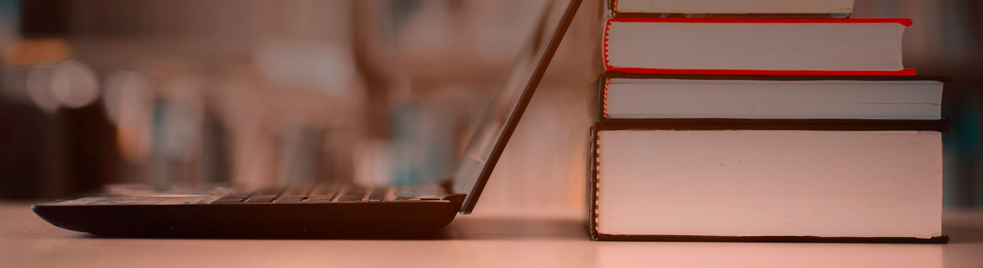 Cuatro libros apilados en la parte derecha y a la izquierda una computadora portátil.