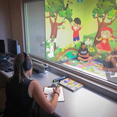 Hombre conversa con un joven, en un aula, desde el ventanal un trabajadora social  analiza el caso